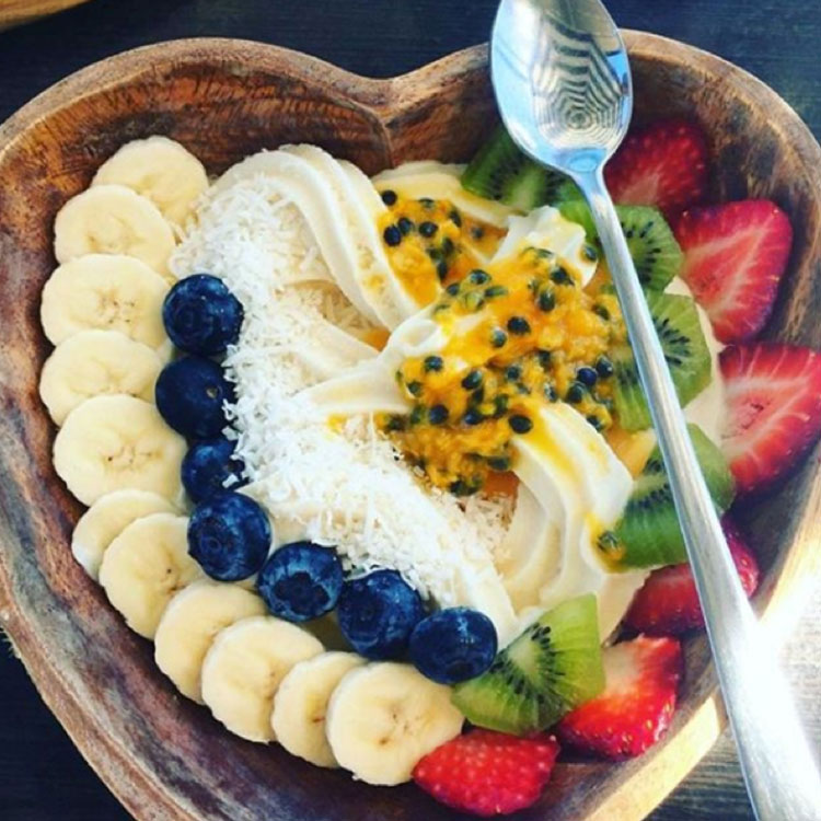 Heart shaped wooden bowl of Cocowhip with bananas, blueberries, passionfruit, kiwi and strawberries