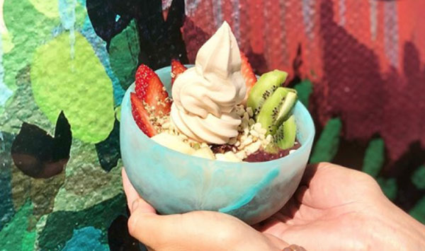 Two hands holding bowl of Cocowhip topped with fresh fruit